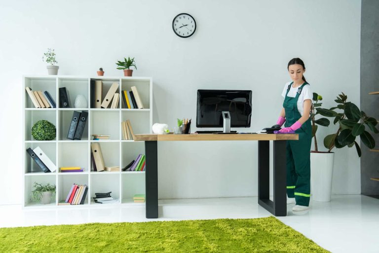 young-cleaning-company-worker-in-rubber-gloves-and-uniform-cleaning-desk-in-modern-office.jpg